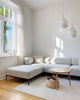 Das modulare noah Sofa in der Konfiguration 3-SITZER MIT CHAISE ECKSOFA mit der Bezugfarbe Sand und Gestellfarbe Schwarz steht in einem minimalistisch eingereichtetem Wohnzimmer.